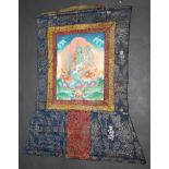A Tibetan thanka wall hanging, the central panel painted with a goddess seated on a lotus leaf,