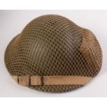 A WWII soldiers 'tin' helmet complete with net cover, shell dressing and original webbing strap,