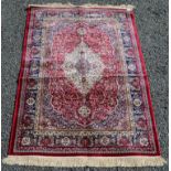 A rug, the red field with an ivory lobed medallion within a blue arabesque border, 171 x 117cm.