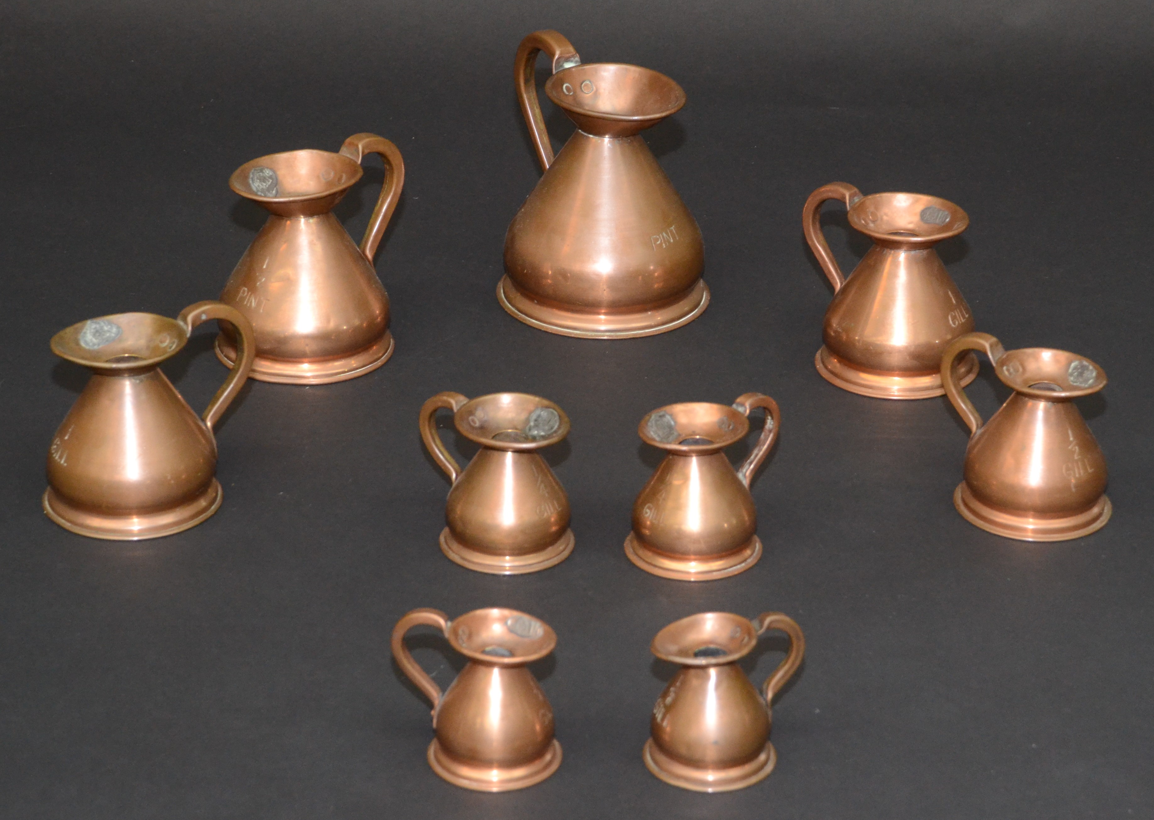 Nine copper bellied measures, ranging from 'pint' to '1/8 gill', largest height 16cm.