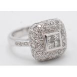 An 18ct white gold ring with a central calibre set four diamond square within a pave set diamond