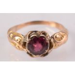 A gold ring set a ruby with scroll chased shoulders.