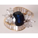 An 18ct gold ring crossover set a central sapphire flanked by rows of graduated baguette diamonds