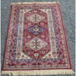 A rug, the red field with three hooked medallions within multiple borders, bearing a label 'Kashmir,
