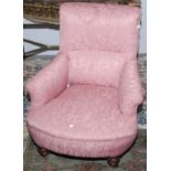 A Victorian low salon armchair upholstered in pink damask fabric on turned legs.