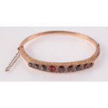 A 9ct gold Victorian style bangle set nine graduated garnets separated by tiny diamonds,