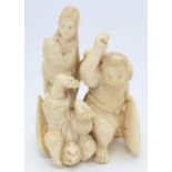 A Japanese ivory okimono group carved as an oni, an upside down kappa, a female figure looking on,