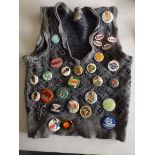 A collection of children's badges, most are tin or plastic all on a short sleeve sweater.