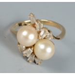 A gold ring with a contemporary cross-over setting with two pearls amongst baguette and brilliant