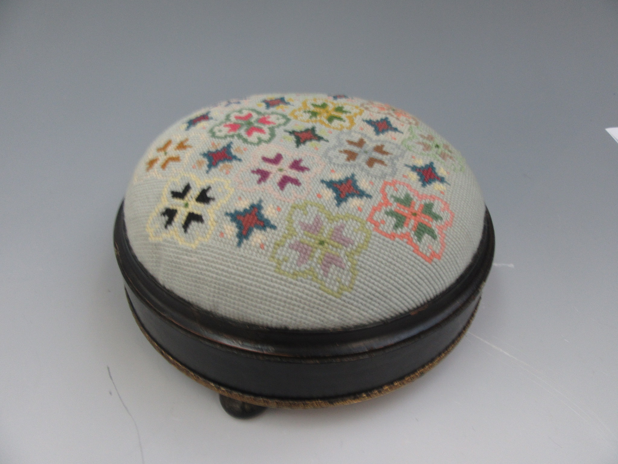 A Victorian ebonised and gilt metal footstool with a circular needlepoint top on bun feet,