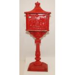 A cast iron red painted post box on stand, the front decorated with figures on horseback,