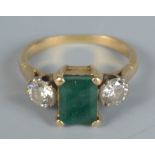A gold ring set with a rectangular emerald and two diamonds.