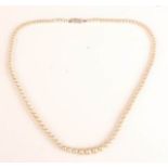 A simulated pearl necklace the engraved gold clasp set with diamonds.
