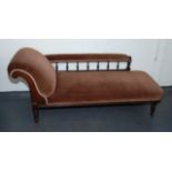 A late Victorian mahogany chaise longue, with padded and spindle filled back, padded arms and seat,