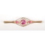 A high purity gold bar brooch set with a 6.8mm diameter pink sapphire, flanked by smaller sapphires.