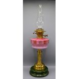 A brass and pink glass oil lamp, the reeded column on a circular plinth pottery base,
