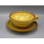A Clive Bowen Studio Pottery cup and saucer, the yellow glaze with green and brown abstract designs,