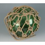 A large green glass fishing float in a rope holder, diameter 26cm approximately.