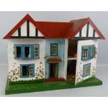 A wooden doll's house, of double fronted twin-gabled form with tin-plate door and windows, the