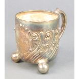 A Victorian repousse silver mug with scroll decoration and vacant cartouche on ball feet London