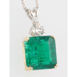 A square cut emerald in a yellow gold mount suspended from a single stone diamond, the main stone