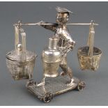 A Chinese white metal condiment in the form of a man carrying 2 baskets and a vase on a wheeled