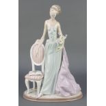 A Lladro figure of a lady standing beside a chair no.1495 14" There are minor chips to the flowers