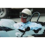 A coloured photograph of Sir Stirling Moss sat in a racing car, signed 6" x 9 1/2"