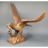 A carved wooden figure of an eagle with wings outstretched, encountering a snake, both set with