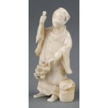A Japanese Meiji period carved ivory okimono of a standing man holding flowers 3"