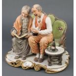 A signed Capodimonte group Ricordi of an elderly lady and gentleman sitting on a couch looking at