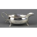 A George II silver sauce boat with chased armorial and floral and shell rim on hoof feet,