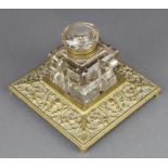 A Victorian square cut glass inkwell raised on a cast brass base with mask decoration 4" x 6" x 6"