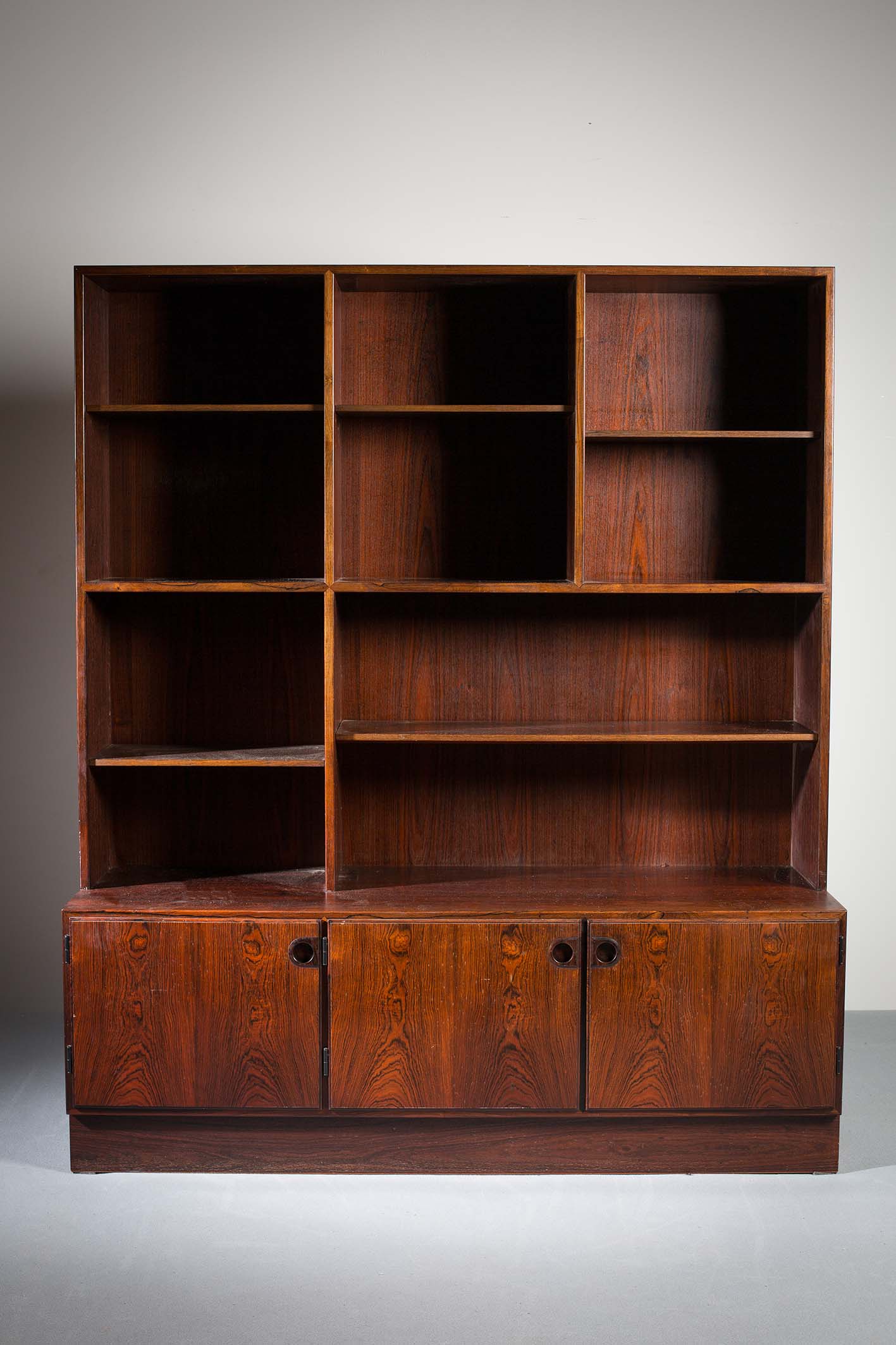 A ROSEWOOD BOOKCASE, DANISH, the open shelved superstructure on a base with three cupboard doors,