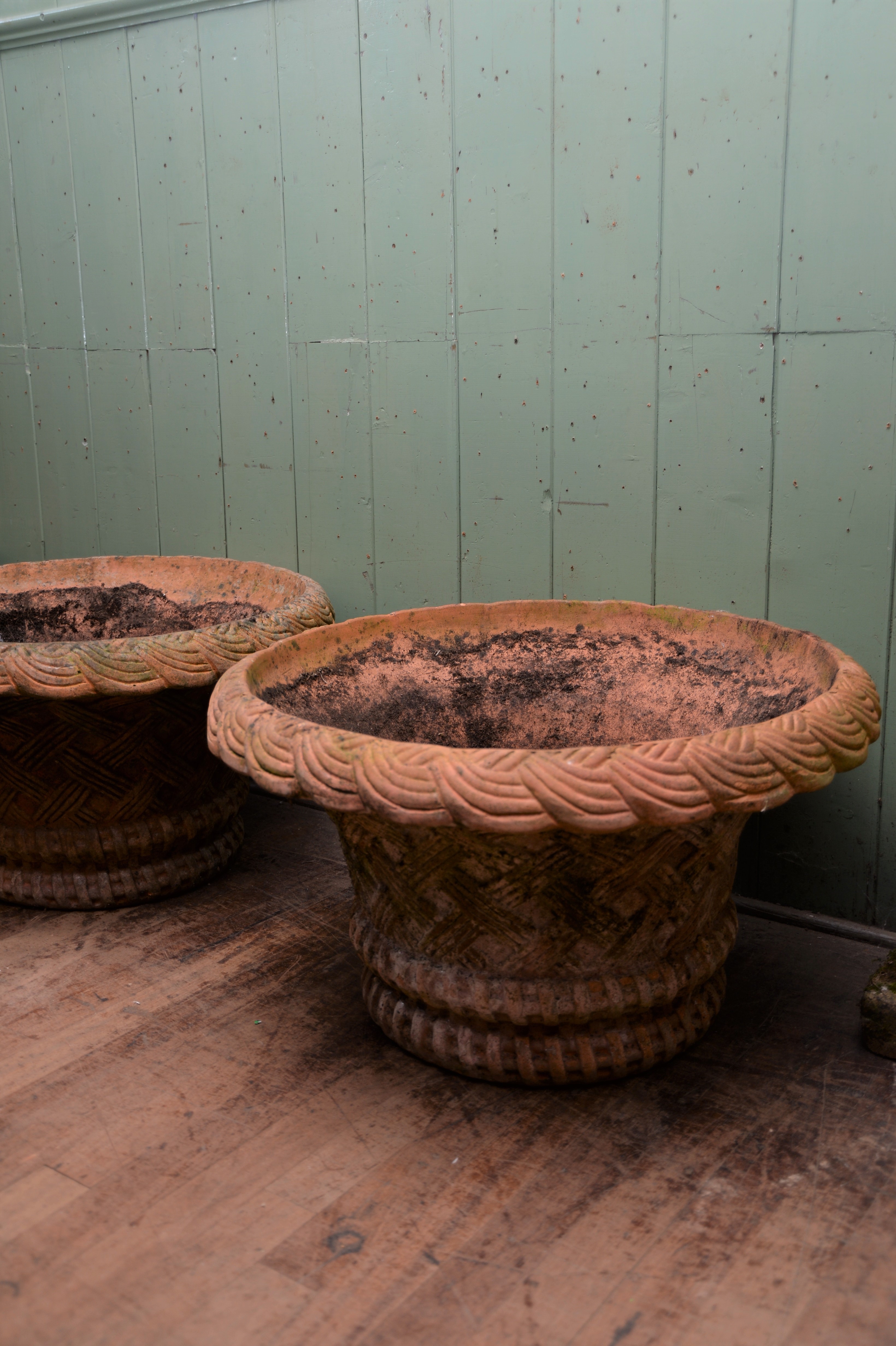 A PAIR OF REPRODUCTION CIRCULAR TERRACOTTA URNS with basket weave sides and turn over rims,