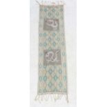 A cotton table runner with pale yellow and green diamond design on a cream ground,