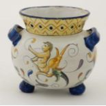 A 19thC French style faience two handled pot on three bun feet, decorated with cherubs in blues,