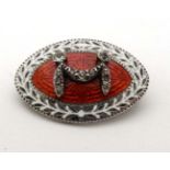 A white metal brooch of elliptical form with white and red gullioche enamel decoration and paste