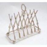 Shooting : A novelty 6 - slice silver plated toast rack, the bars formed as crossed guns / rifles .