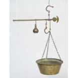 Old brass hanging scales with large pan to one end and weight to other.