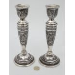 A pair of white metal and silver plated candlesticks with floral and figural decoration.