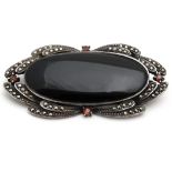 A 20thC silver brooch with central black enamel cabochon bordered by marcasites and red stone.