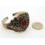 A silver bangle bracelet with gilt decoration and set with red white green and purple stones