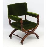 A 19thC Neogothic green velvet upholstered X-frame upholstered open armchair on casters.