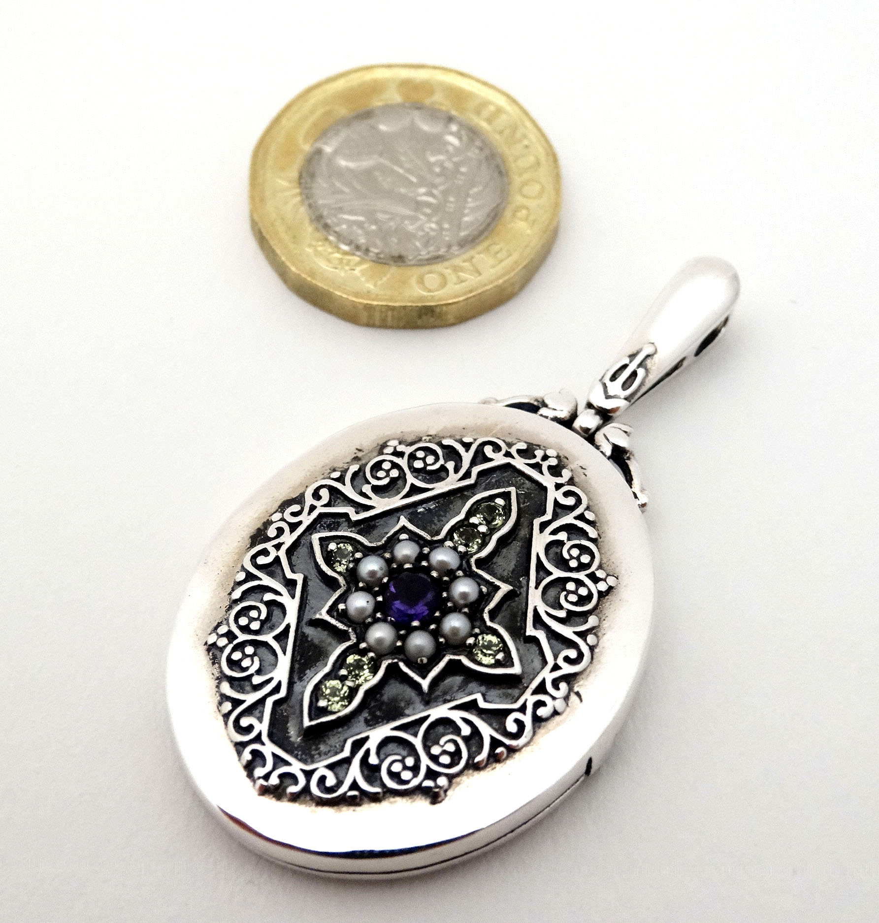 A Sterling silver locket set with peridot, amethyst and seed pearls.