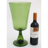 A large green glass pedestal vase formed as an oversized drinking glass.