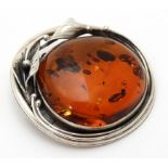 A white metal pendant / brooch set with amber cabochon within a floral scrolling mount.