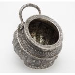 A white metal sugar bowl of stylised scuttle form profusely decorated and with snake formed handle.