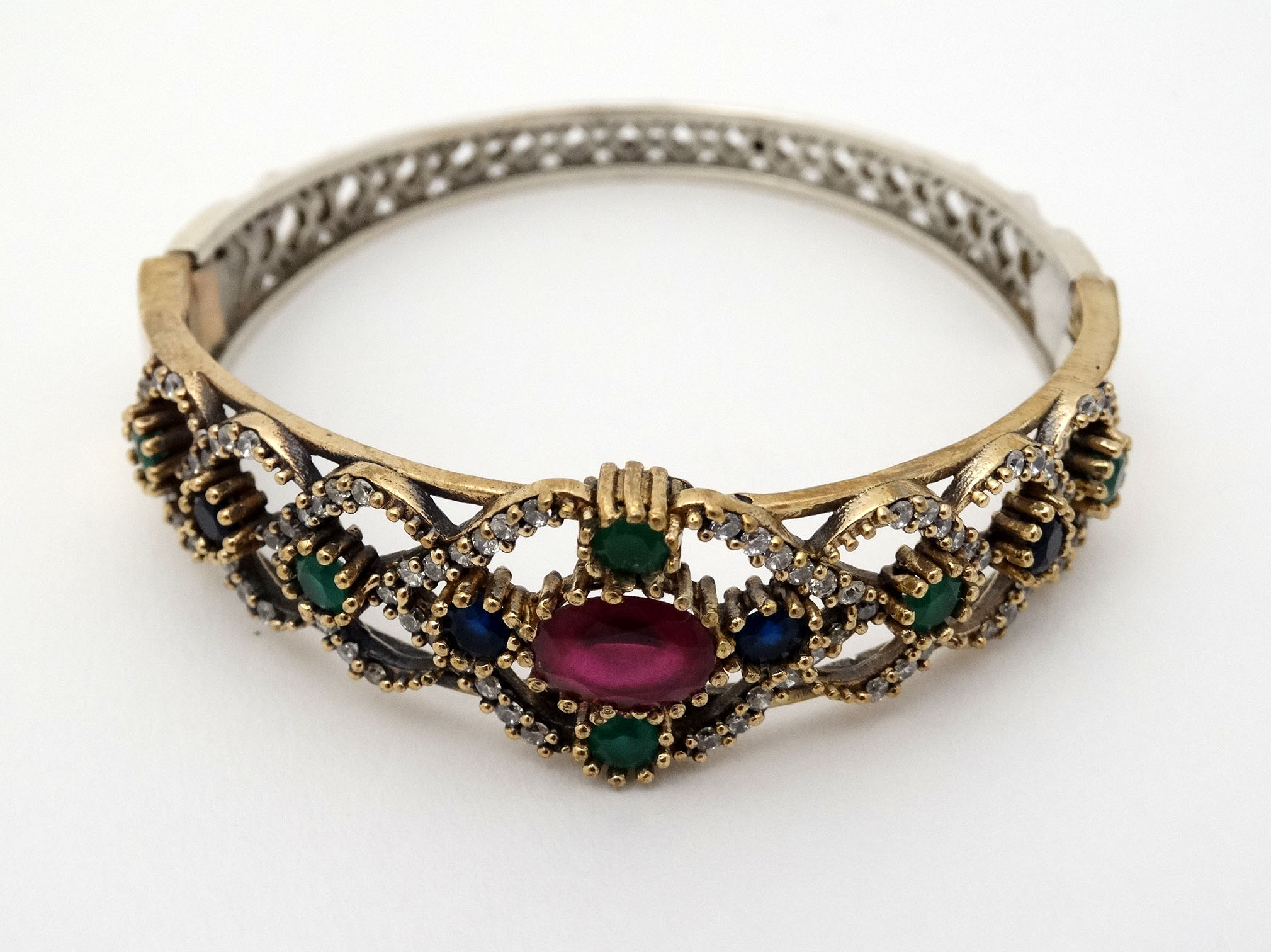 A silver bracelet of bangle form with gilt decoration and set with red blue and white stones