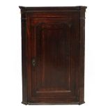 A Georgian oak hanging corner cupboard with shaped panel door.